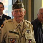 Three veterns,two of which are in uniform, gather in this yellow room