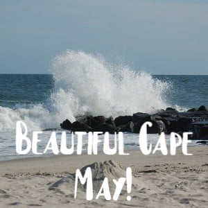 Large white wave crashing against black rocks by a sandy beach