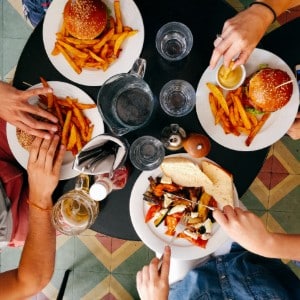 Four people sitting around a black circular table with burgers and fries on white plates