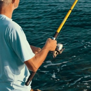 Man in light blue t-shirt holding a yellow fishing rod in open water