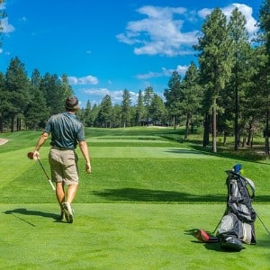 Man in beige shorts standing on the fairway of a golf course next to his golf bag