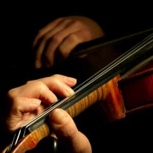 Up close view of two hands playing a brown violin with a black background