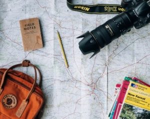 A map open on a table with a long-lensed camera, pencil, notebook, bag and brochures