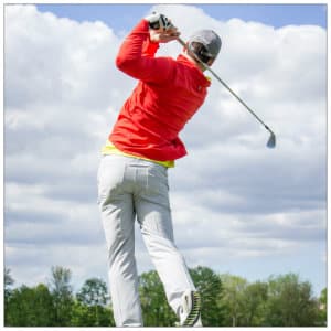 Man in a red jacket and white pants swinging a golf club - photo by courtney prather www.unsplash.com