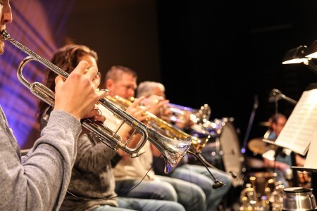 A line of musicians playing various brass instruments while looking at sheet music 