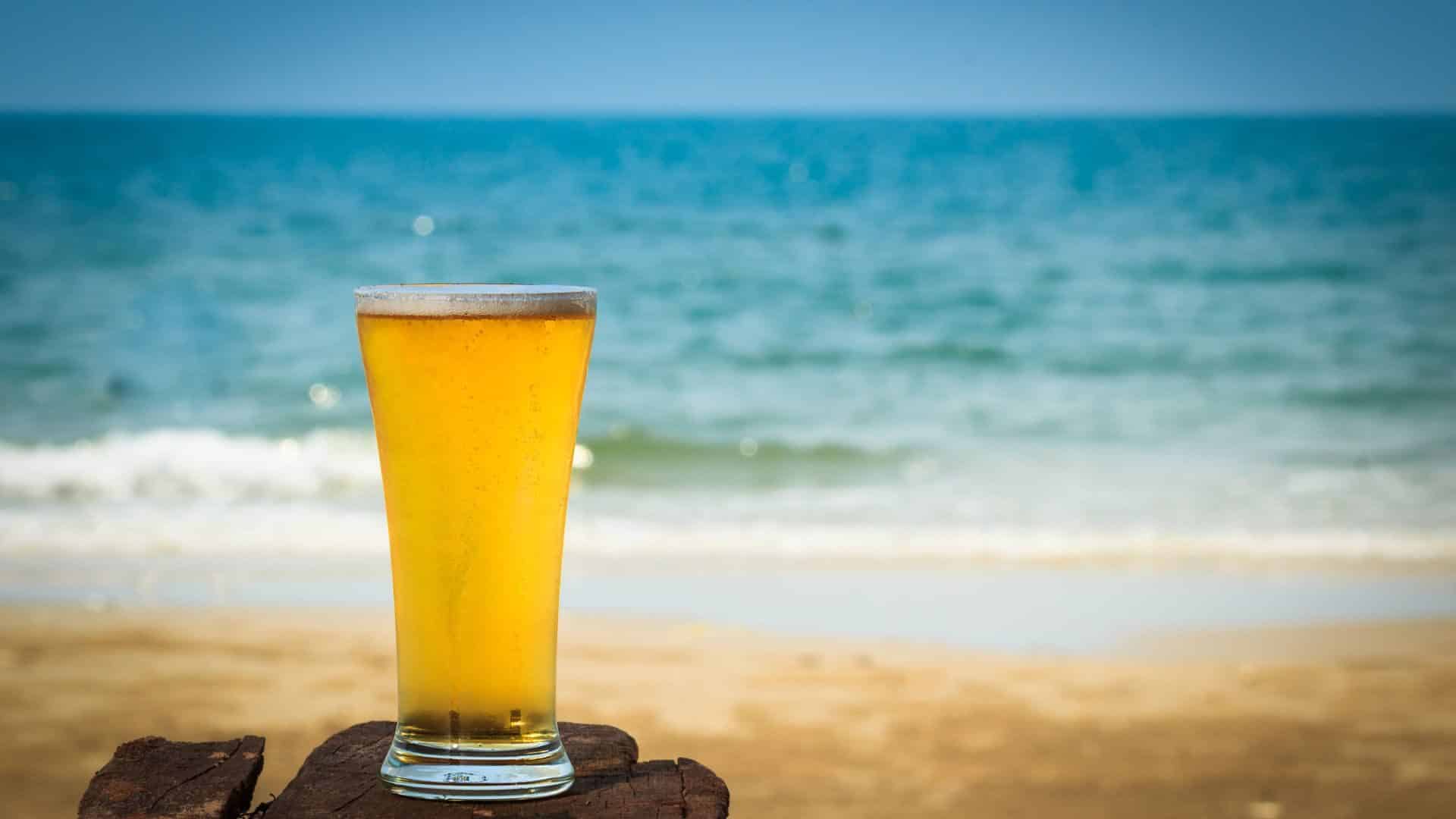 tall glass of beer sitting by the edge of the beach
