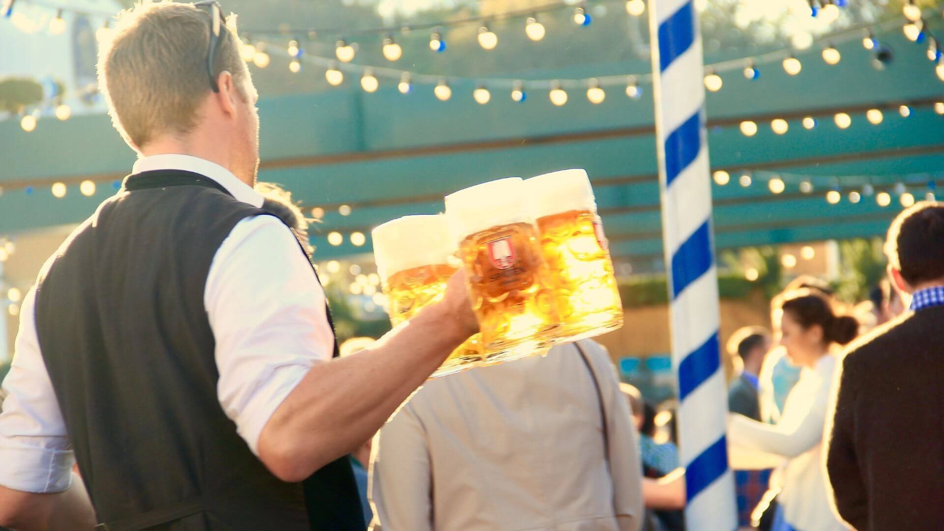 Waiter holding multiple steins of beer serving to crowd with lights hanging above