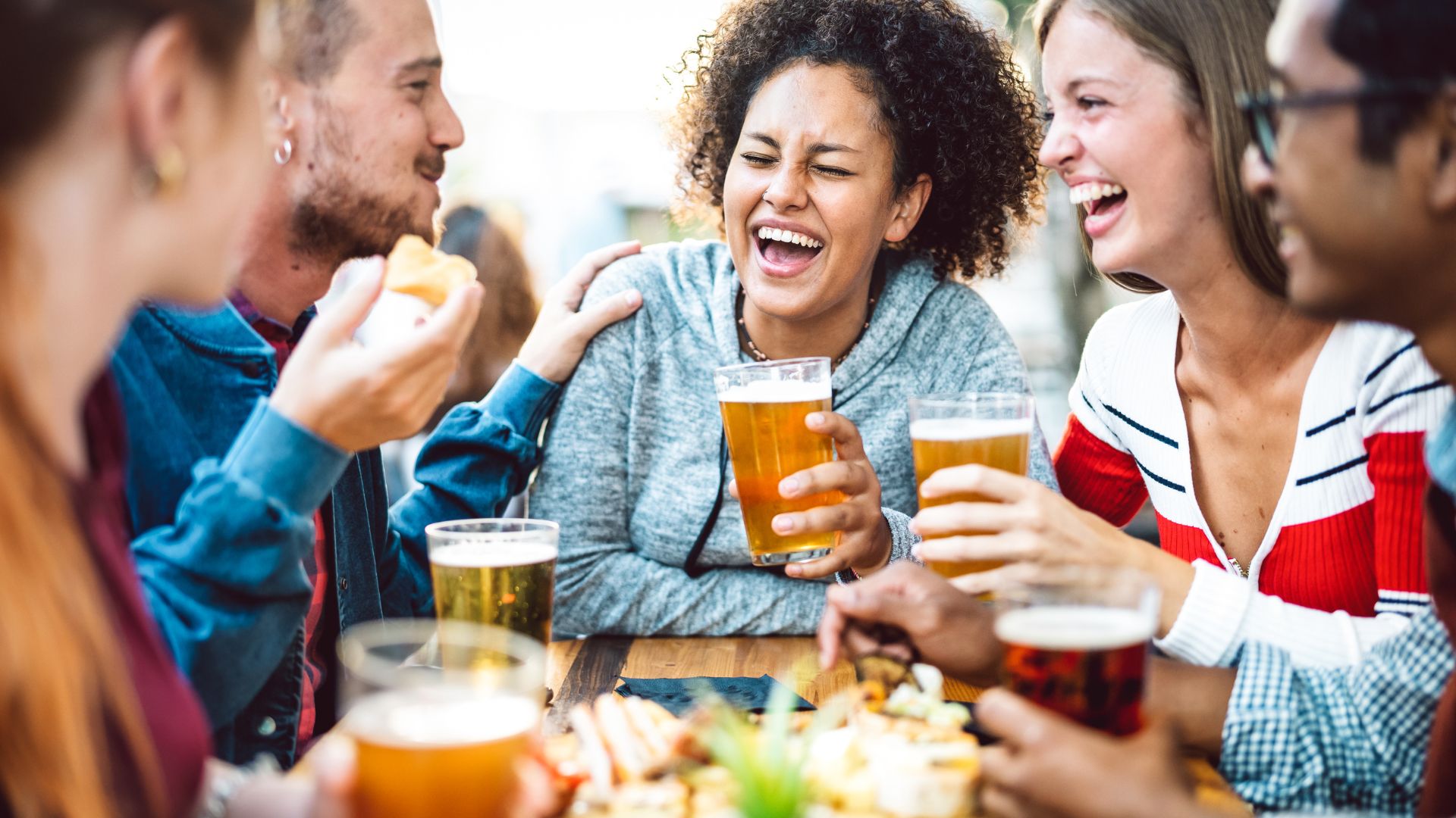 Friends gathered around an outdoor table having dinner and drinking craft beer.