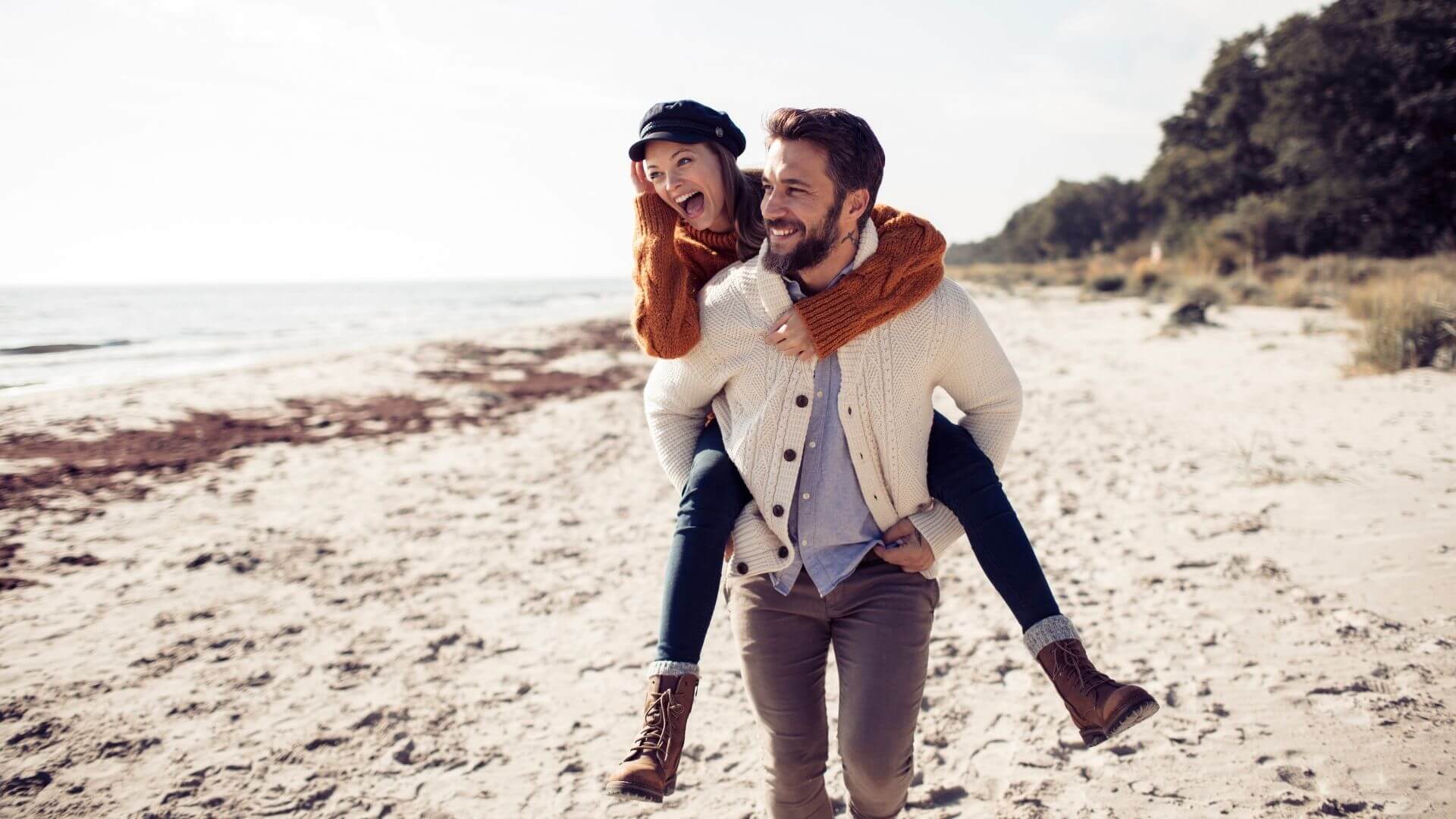 couple walking and laughing on sandy shoreline dressed warm