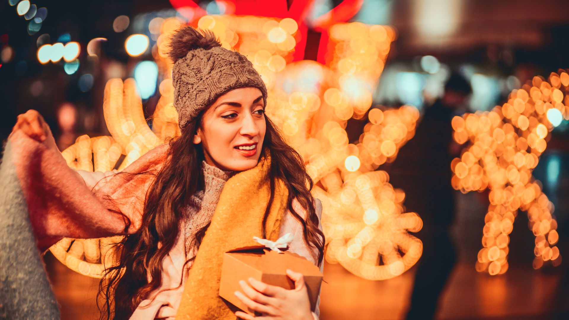 Woman in winter coat with scarf outside shop with bright sparkling lights