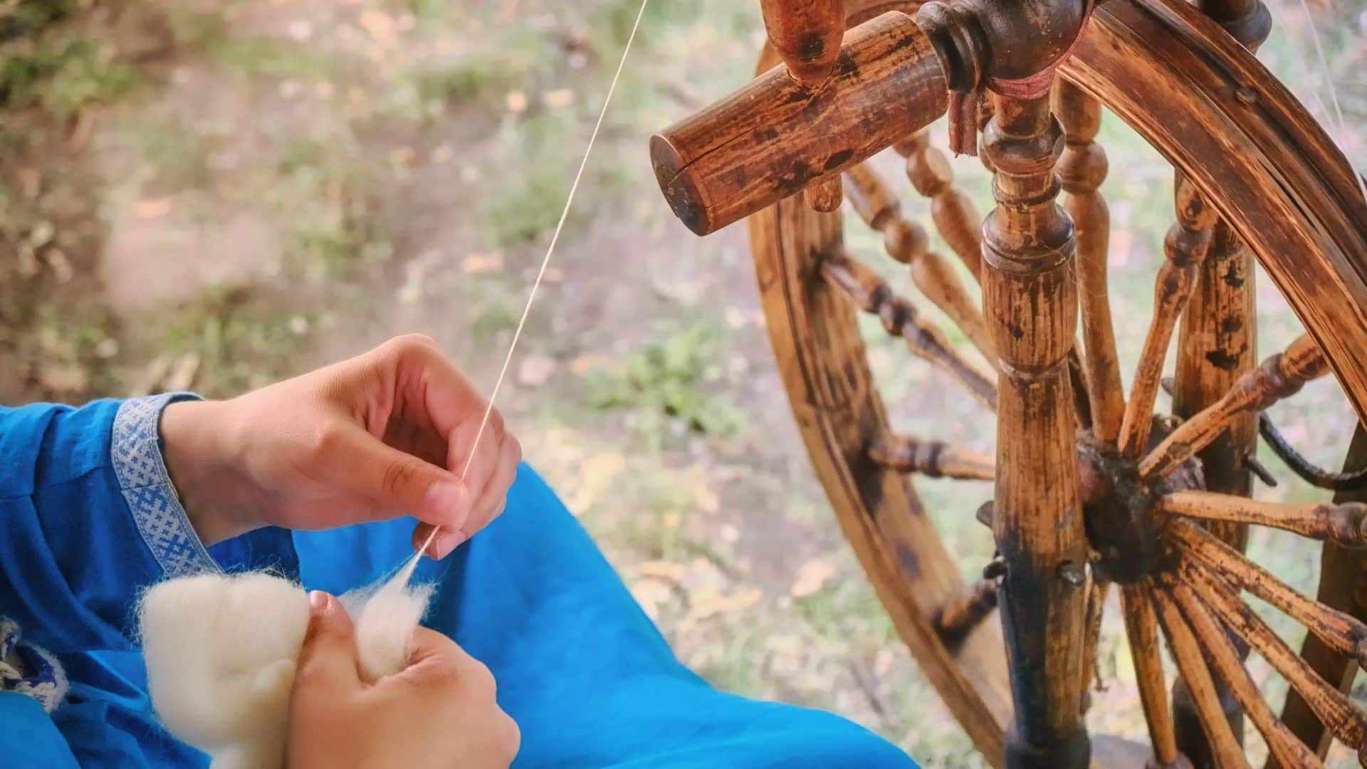 hands holding wool and operating manual spinning wheel