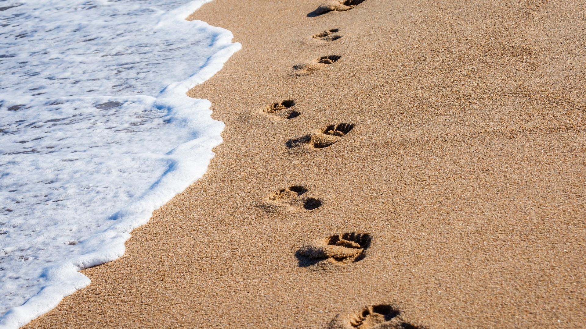 footprints on the beach with waves approaching