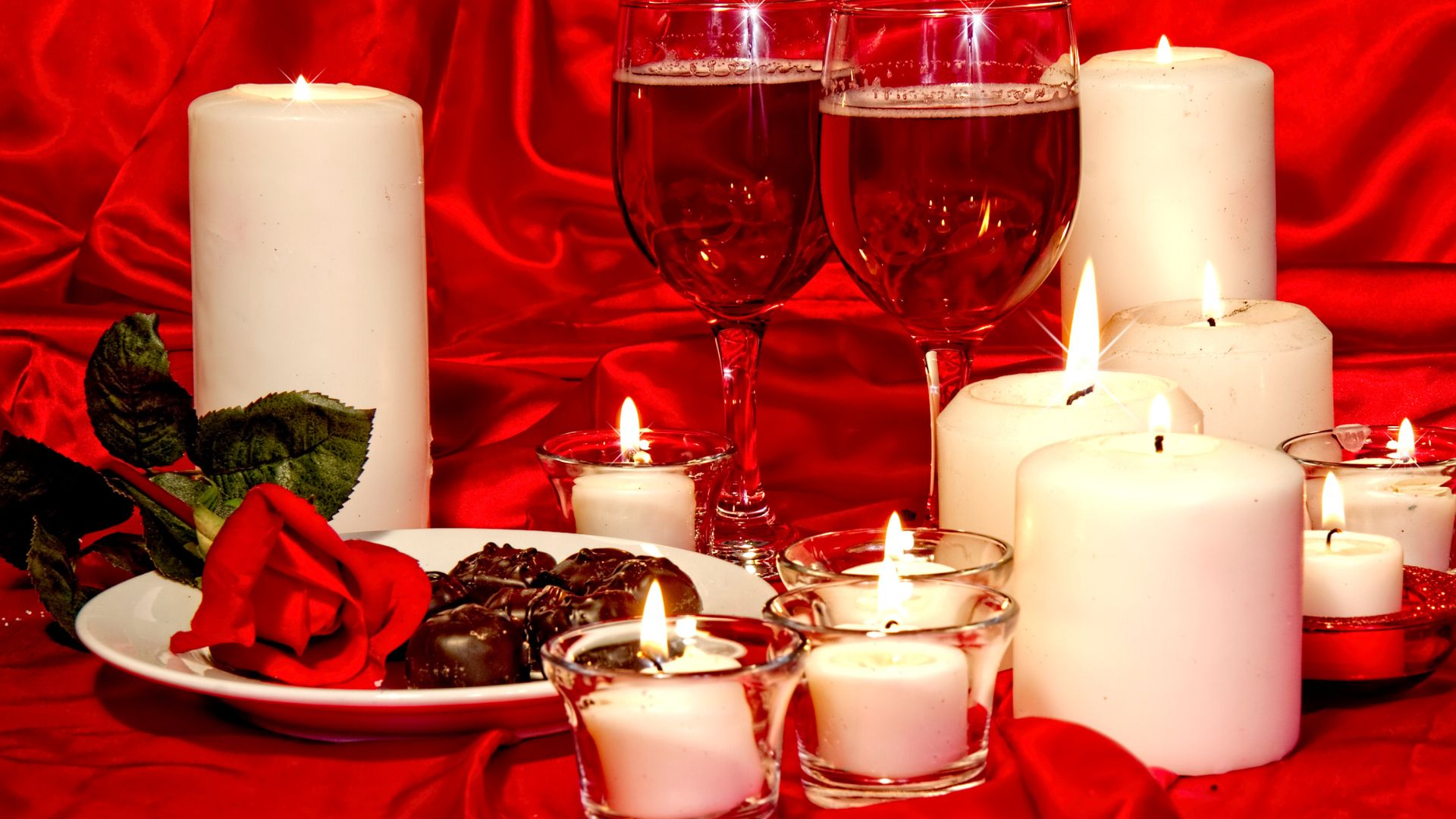 Red draped fabric with two glasses of wine, chocolates and flowers