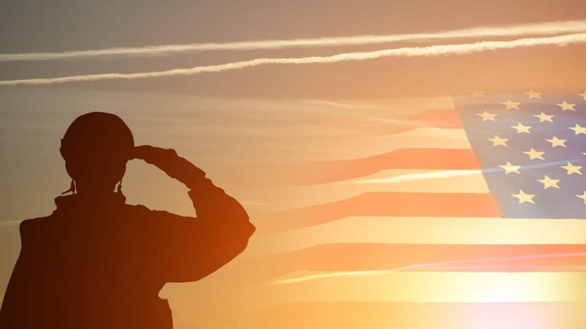 Soldier with helmet saluting into sunlight with american flag in background