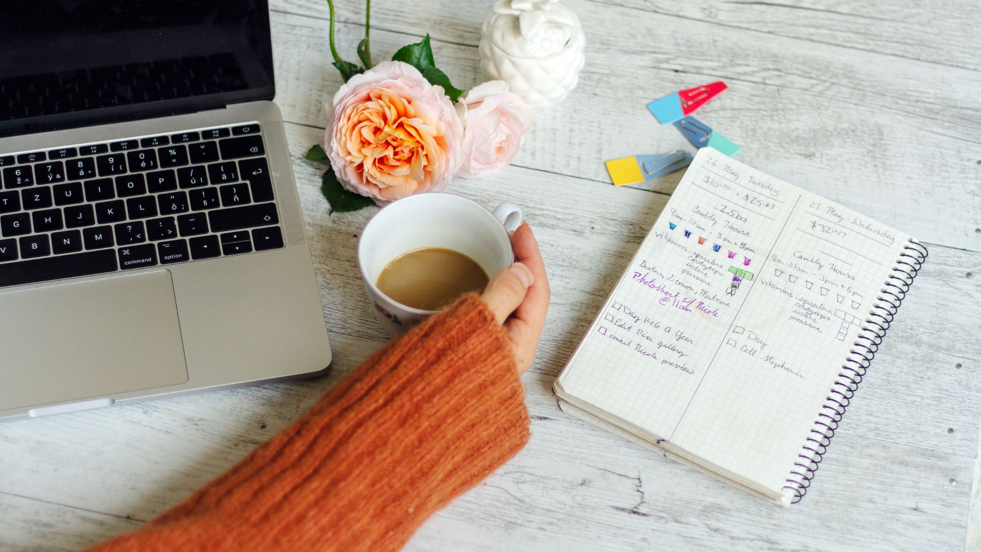 home work station with computer, coffee, woman's hand, flower