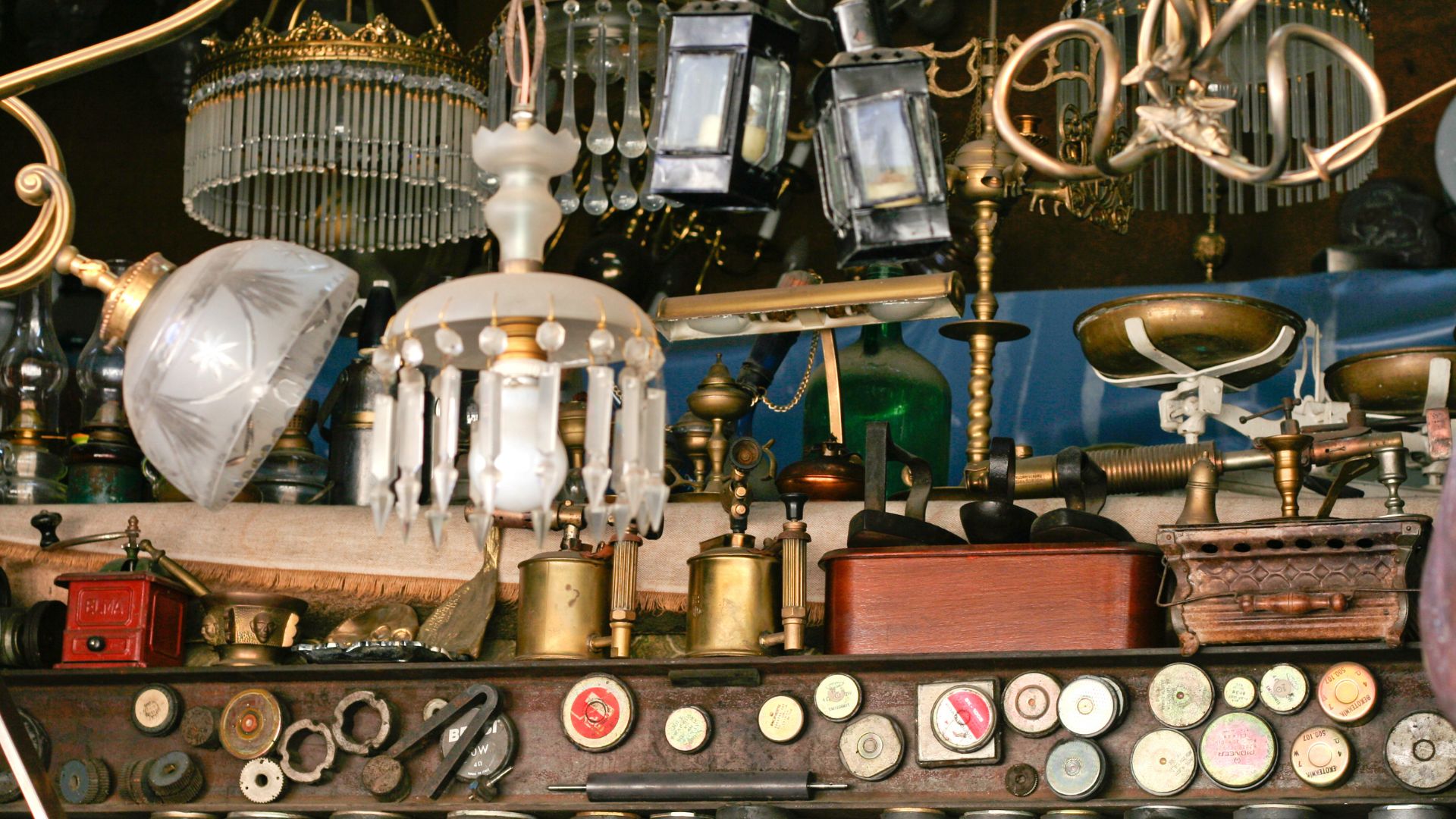  Items at an antique booth, including multiple chandeliers, a coffee grinder, an oil can, a scale, and buttons. 