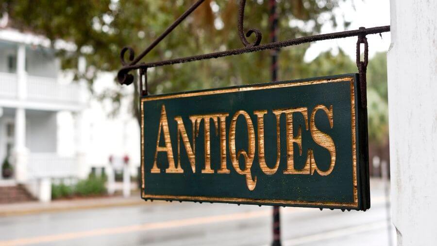a green and gold sign reading antiques hangs outside a shop
