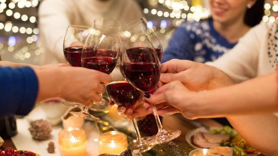 a group of people clink glasses of red wine together at a festive table with candles and twinkling lights