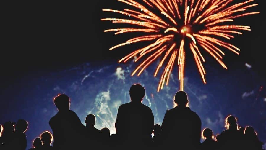 Crowds gather under the night sky to watch a colorful fireworks celebration.
