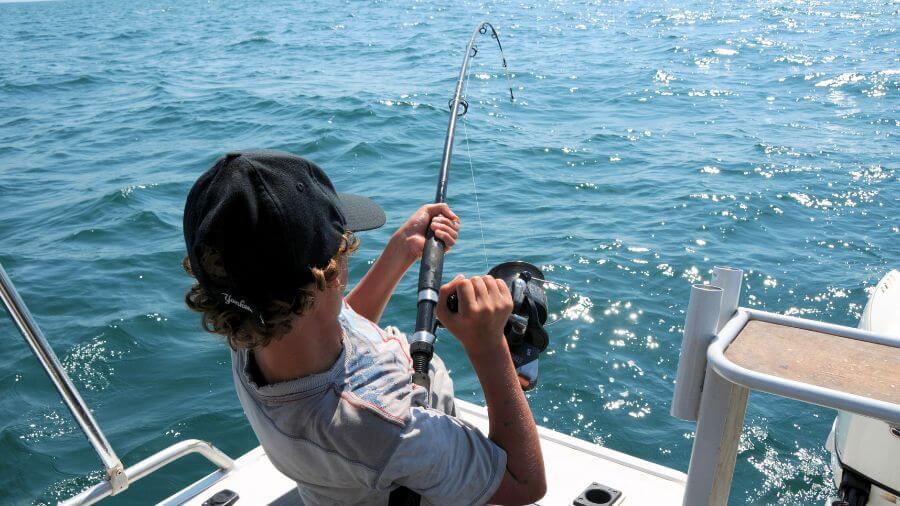A young angler reels in a catch while fishing on open water during a sunny day.