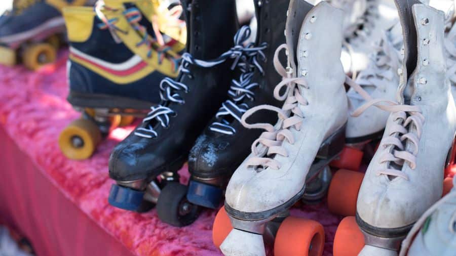 Half dozen pairs of white and black roller skates sitting on a bright pink padded bench.