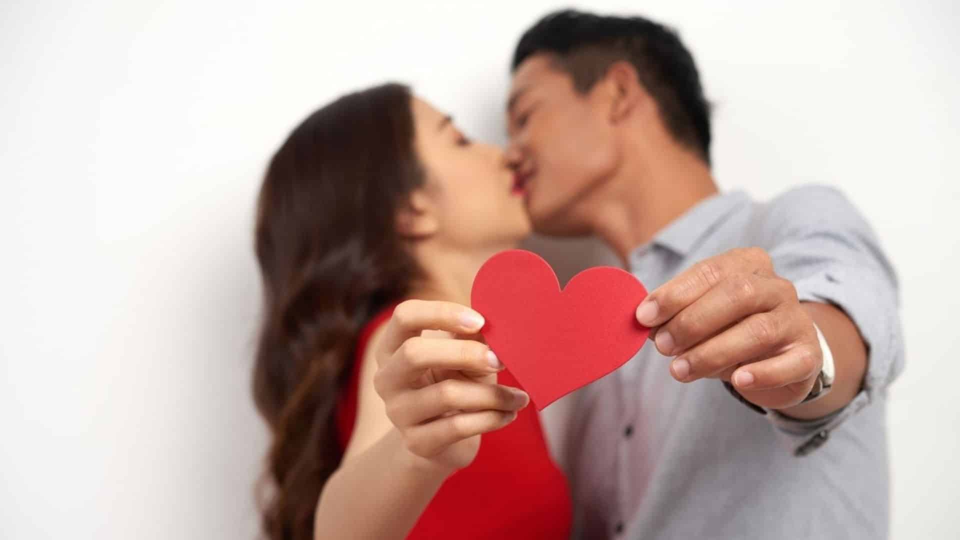 A man and woman kissing while holding up a red paper heart