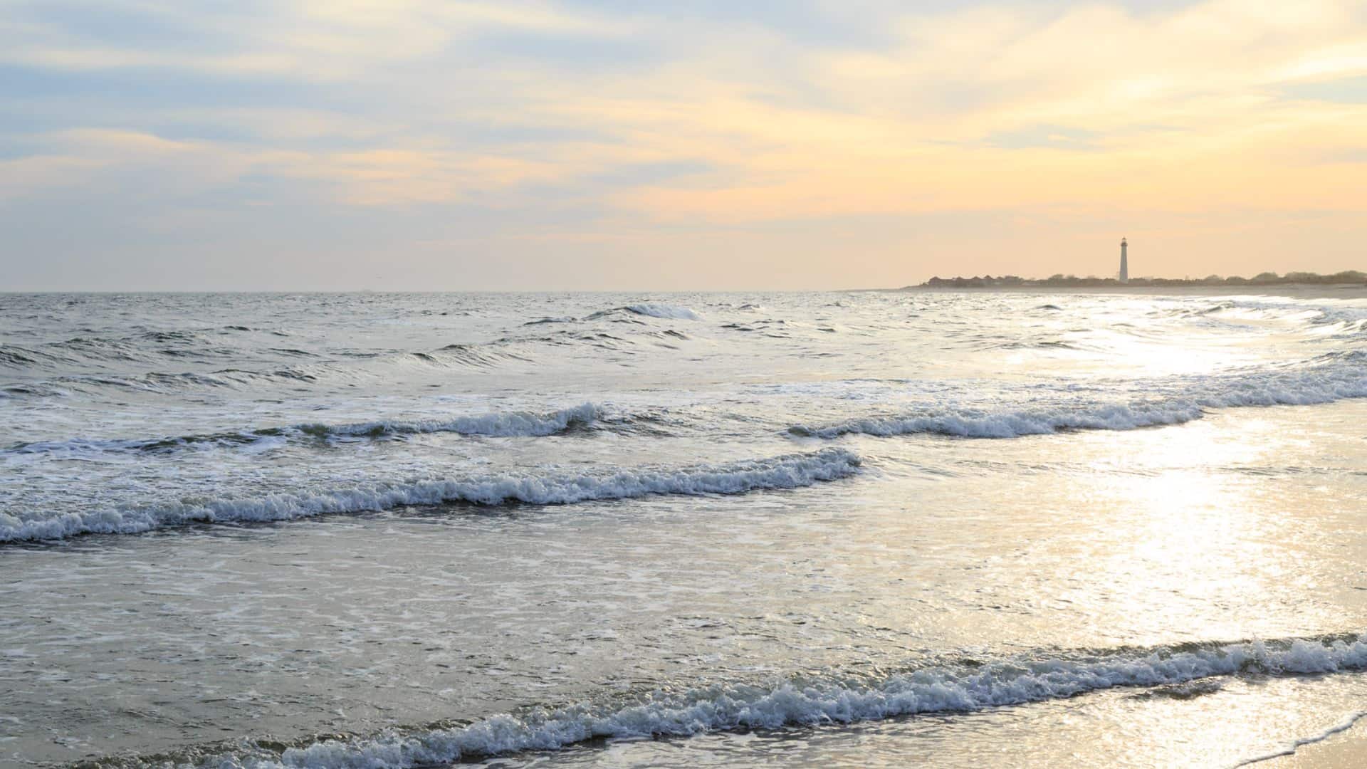 Soft waves rolling on a sandy beach with a lighthouse off in the background