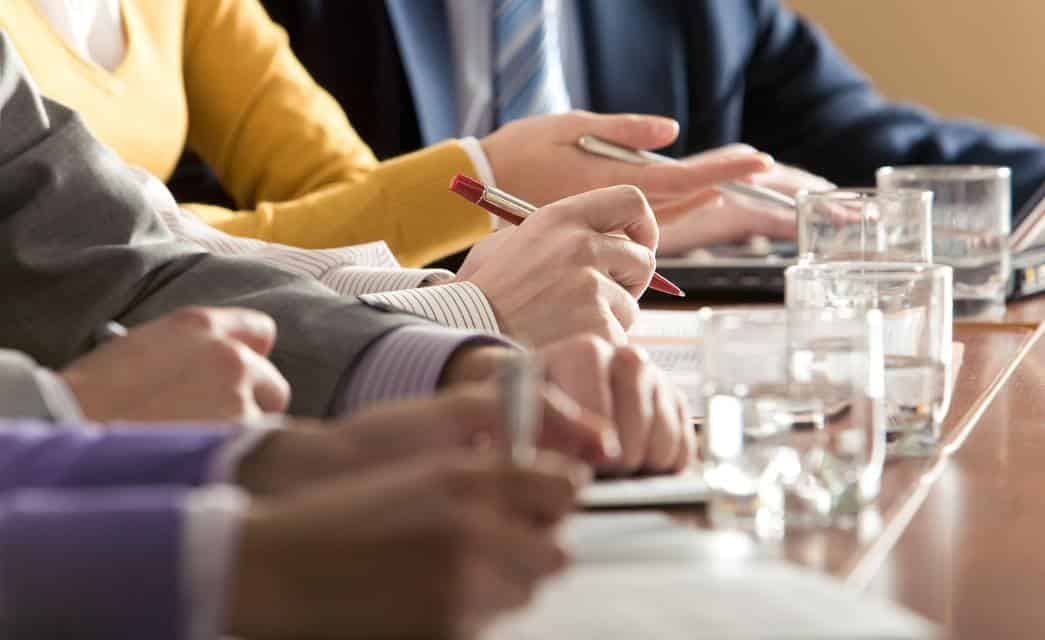 Close up view of arms of business people holding pens and sitting at a table with glasses of water