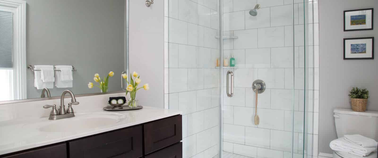 Bathroom with white-tiled flooring and shower, and dark wooden vanity with marble top