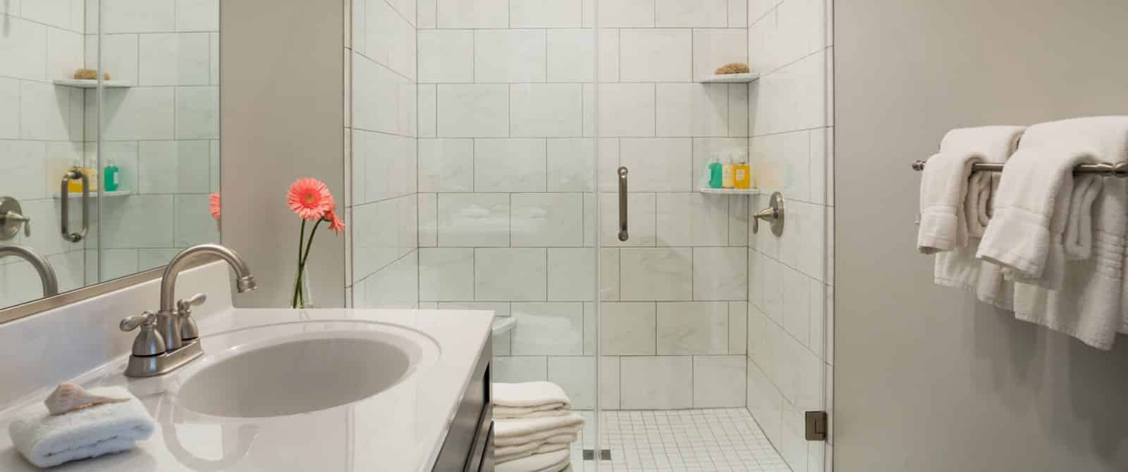 Bathroom with large walk-in marble-tiled shower, dark wooden vanity with marble top and sink, and large mirror