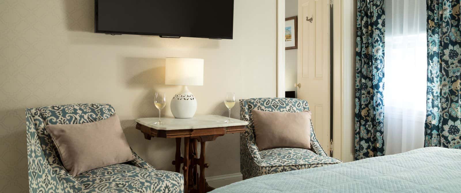 Bedroom's sitting area with upholstered chairs, table with marble top, and wall-mounted flat-screen TV