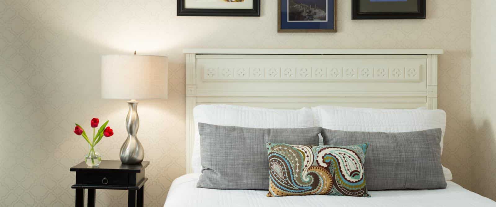 Bedroom with light-colored ornate headboard, white bedding, gray pillows, and dark wooden nightstand