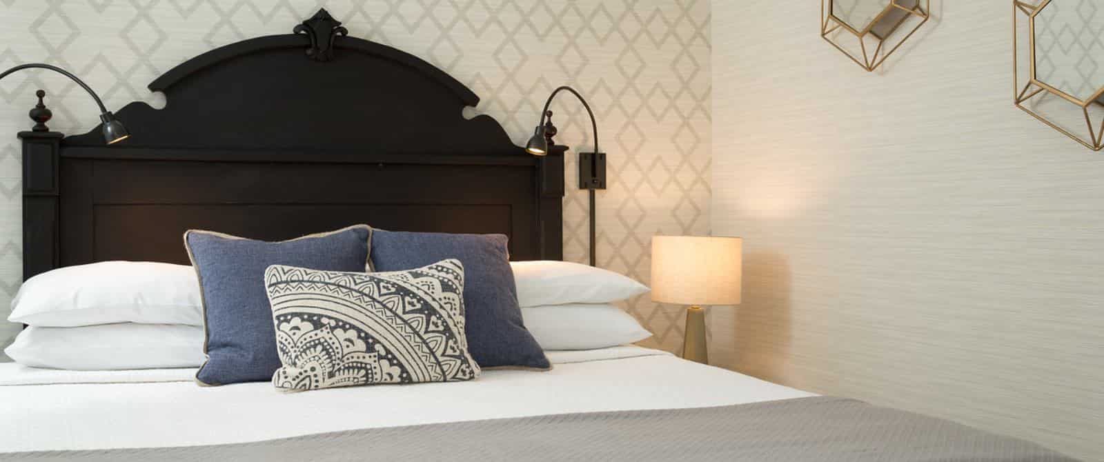 Bedroom with dark wooden headboard, white bedding, gray blanket, denim pillows, and modern wallpaper