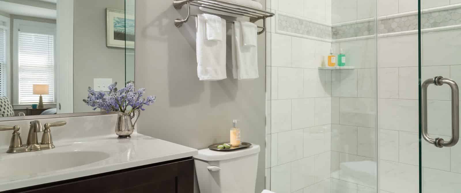 Bathroom with white-tiled shower, dark wooden vanity with marble top, and large mirror