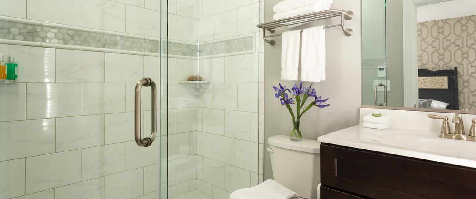 Bathroom with large walk-in marble-tiled shower, dark wooden vanity with marble top and sink, and large mirror