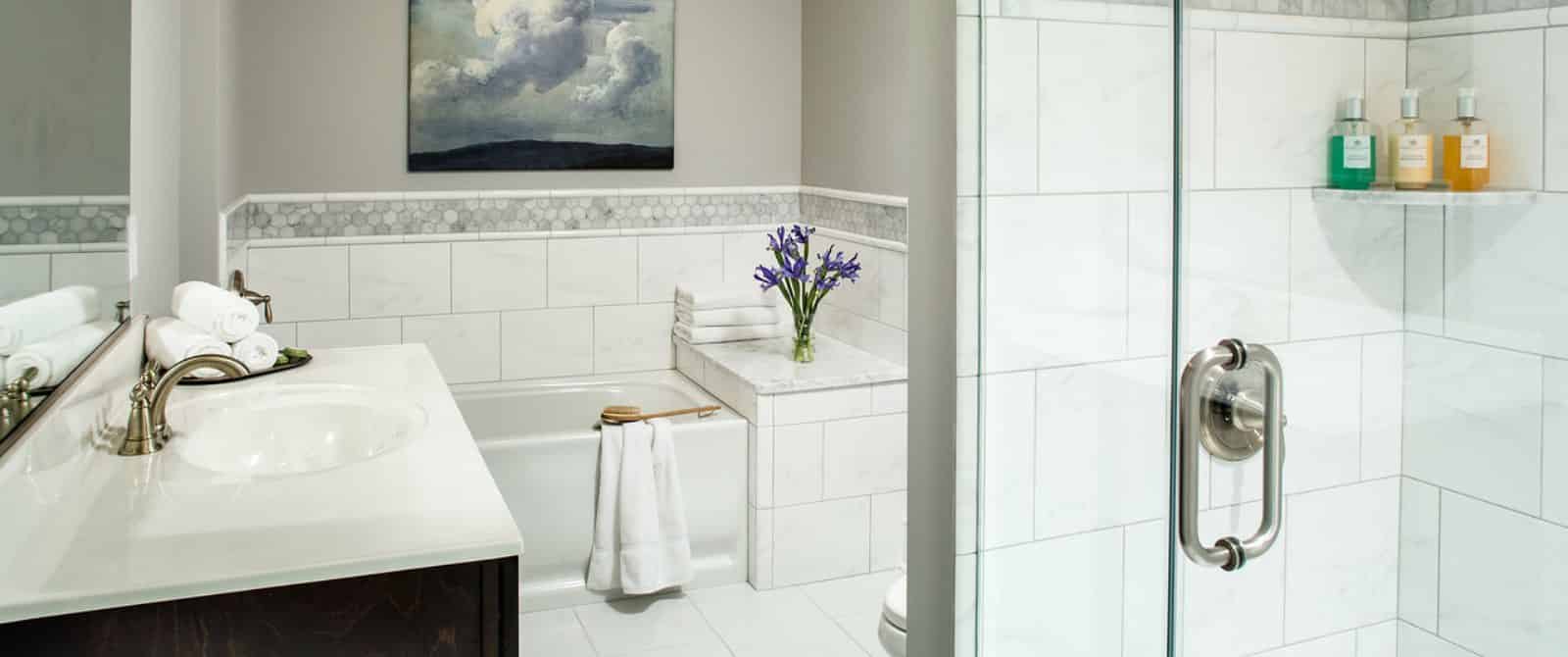 Bathroom with white-tiled flooring, shower, and tub, and dark wooden vanity with marble top