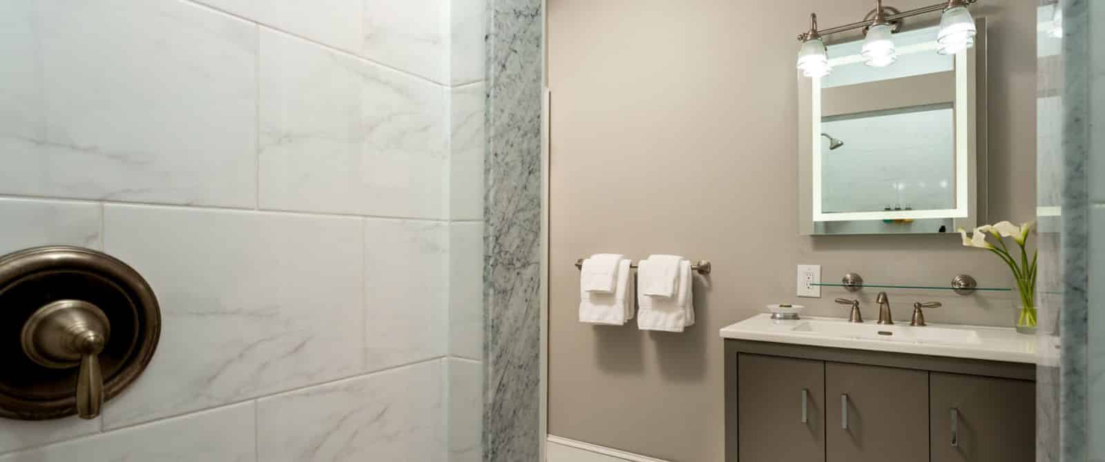 Bathroom with marble tile, dark taupe vanity, mirror, and light taupe walls