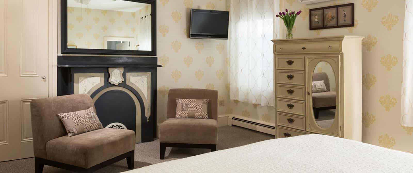 Sitting area with brown upholstered chairs, dark wooden mantel, large mirror, wall-mounted TV, and antiqued dresser