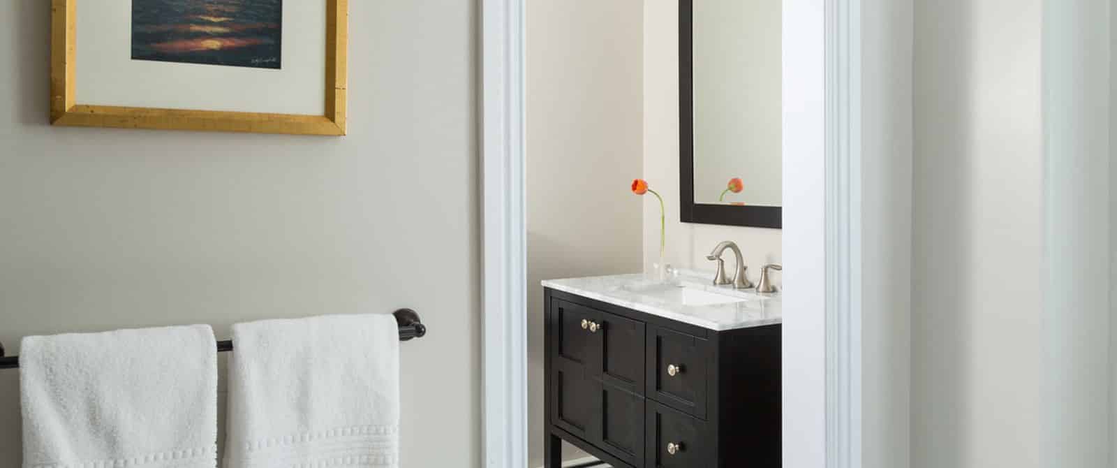View into bathroom with dark wooden vanity, marble top, and large framed mirror