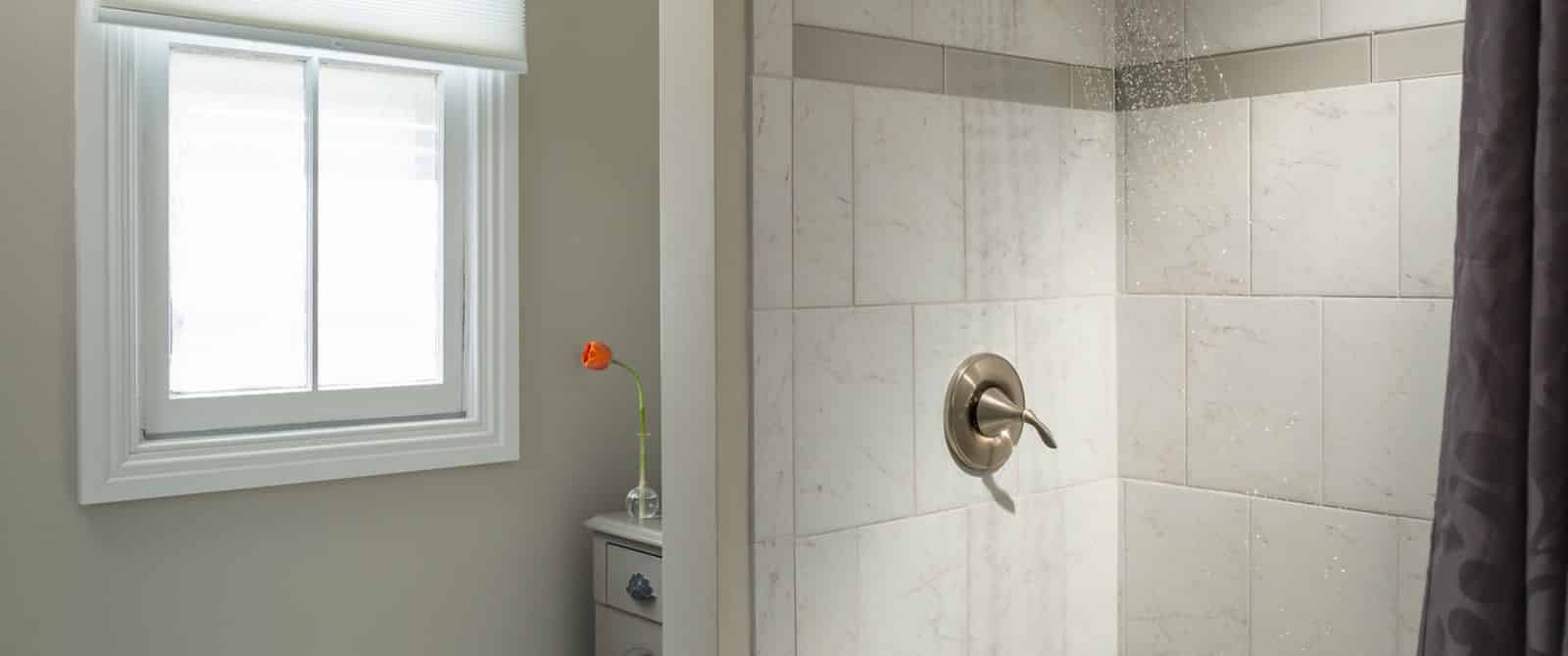 Bathroom with marble tiled shower and light gray cabinet with marble top and glass vase with a single orange tulip