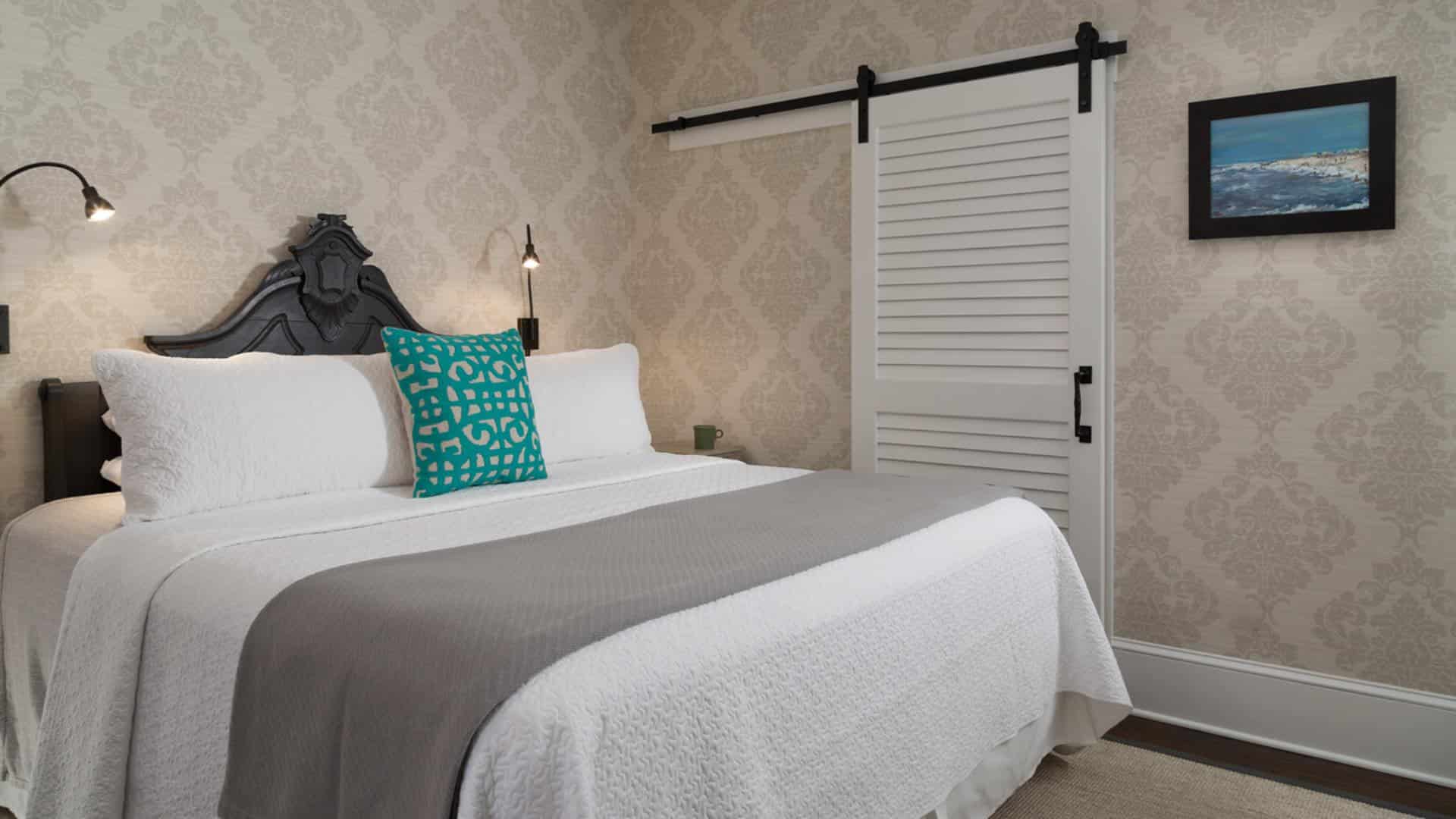 Bedroom with dark wooden ornate headboard, white bedding, gray blanket, hardwood flooring, and ornate wallpaper