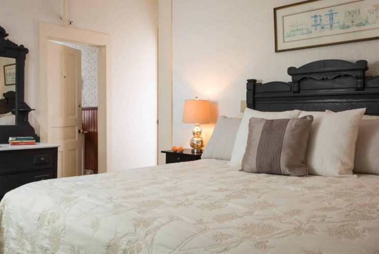 Bedroom with dark wooden ornate headboard, matching dresser with mirror, cream-colored bedding, and dark wooden nightstand