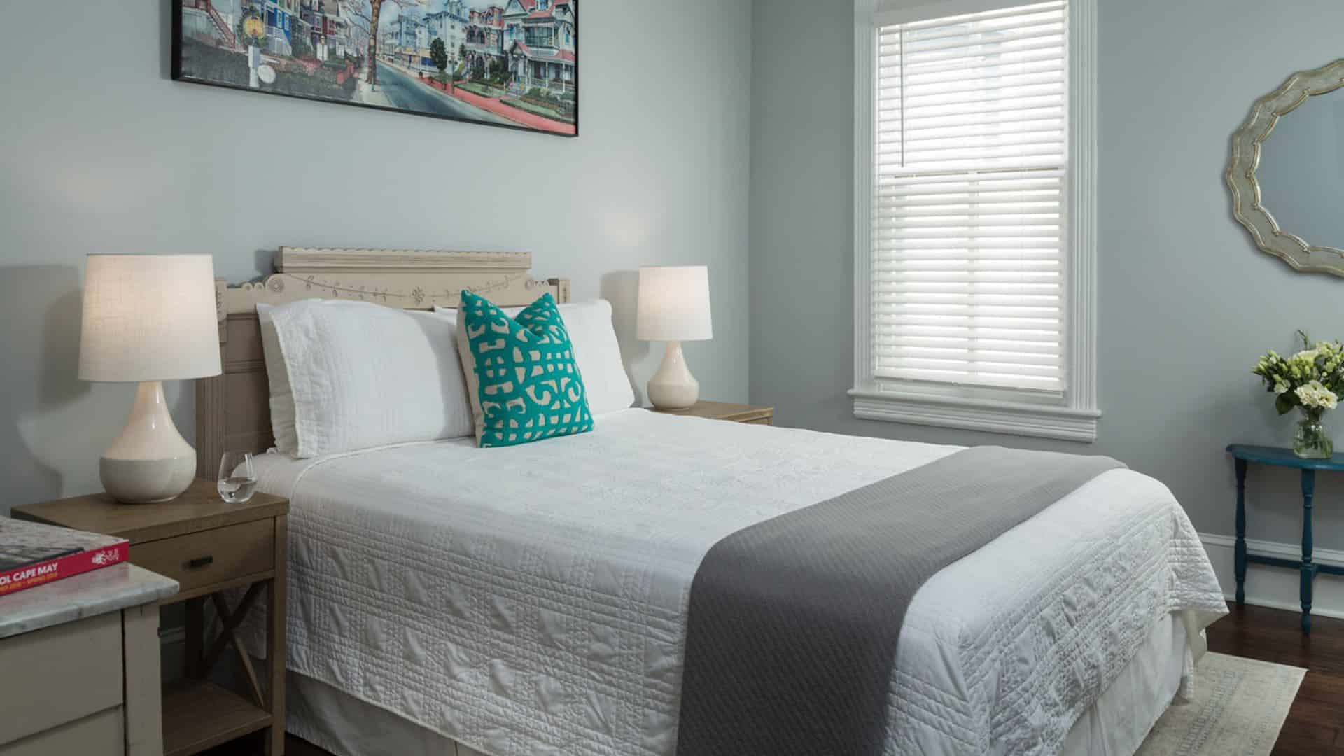 Bedroom with light-colored ornate headboard, white bedding, gray blanket, hardwood flooring, and light gray walls