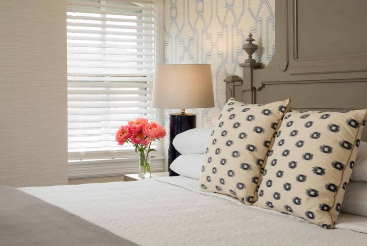 Bedroom with large gray headboard, white bedding, gray blanket, yellow and black pillows, and vase full of pink flowers