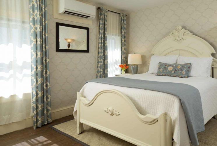 Bedroom with light wooden ornate headboard, matching footboard, white bedding, gray blanket, hardwood flooring, and mirror