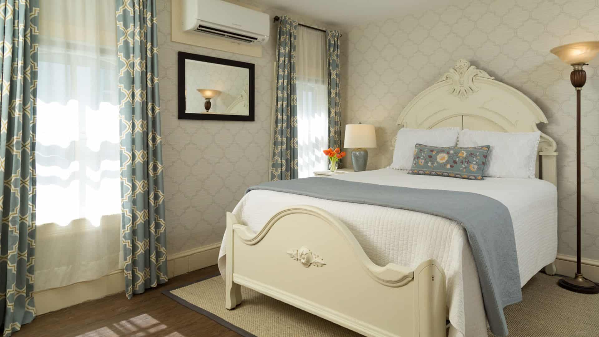 Bedroom with light wooden ornate headboard, matching footboard, white bedding, gray blanket, hardwood flooring, and mirror