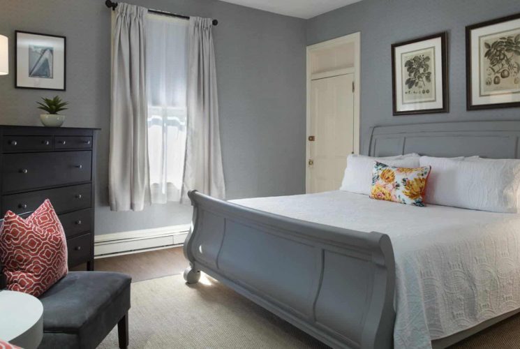 Large bedroom with gray wooden sleigh bed, white bedding, gray upholstered chair, and dark wooden dresser