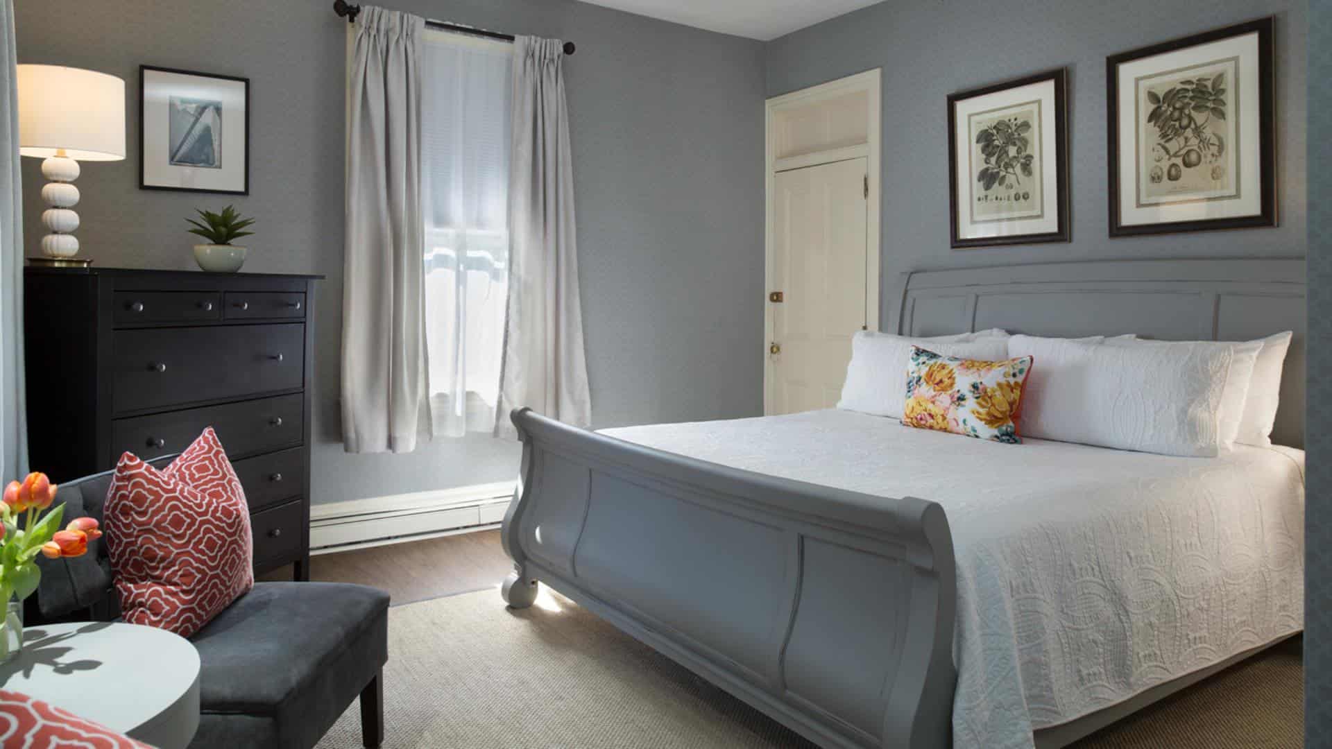 Large bedroom with gray wooden sleigh bed, white bedding, gray upholstered chair, and dark wooden dresser