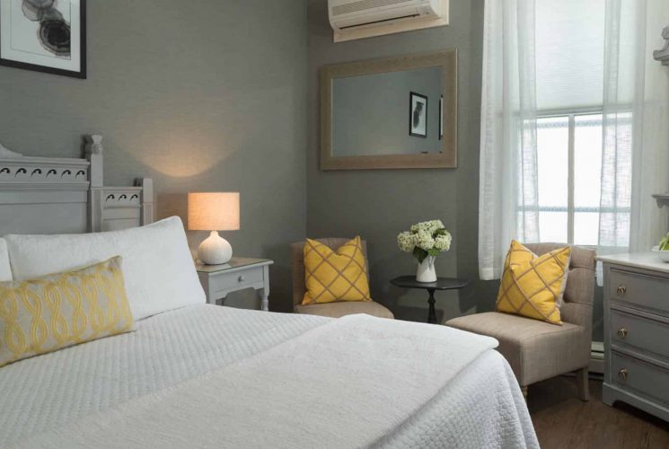 Bedroom with large gray headboard, white bedding, yellow pillows, hardwood flooring, gray walls, and gray dresser with marble top and mirror