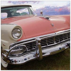 Shiny pink and white ford fairlane classic car sitting on grass with sunset sky behind